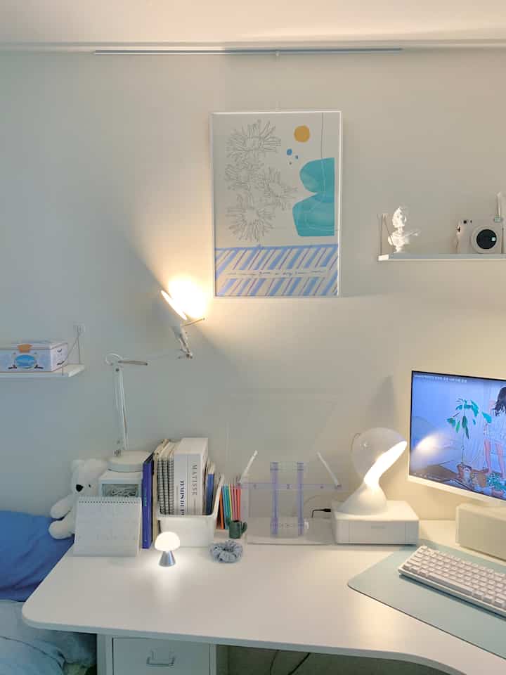 White and blue toned home office featuring a desk, poster, and lighting in a clean design