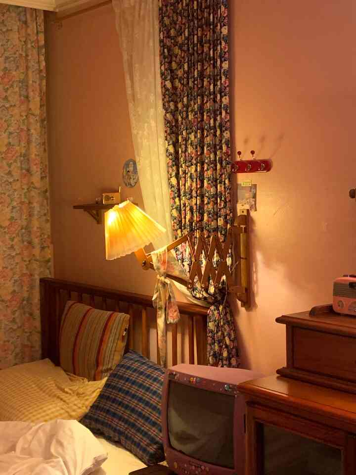 Cozy bedroom with warm purple and wood tones, featuring floral curtains and a retro TV, creating a nostalgic atmosphere