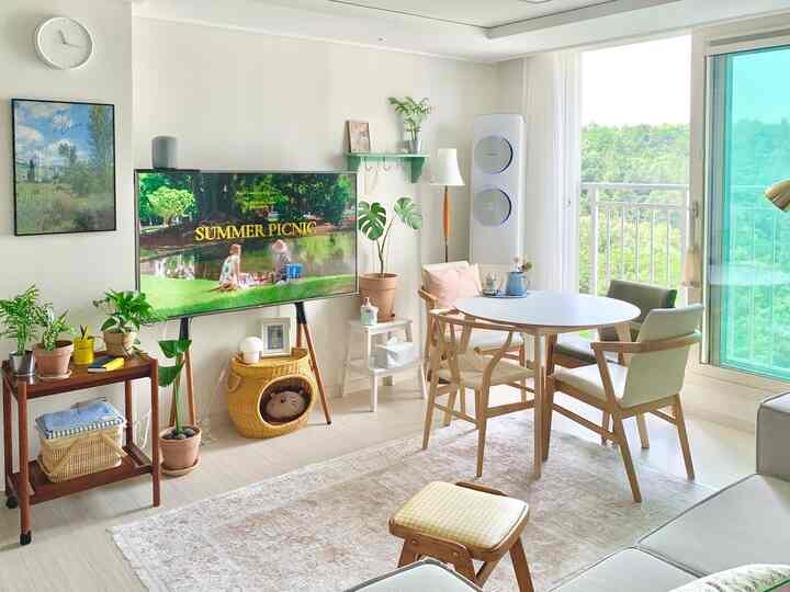 White and wood tone living room featuring round dining table, assorted plants, and rattan cat house in a natural modern setting