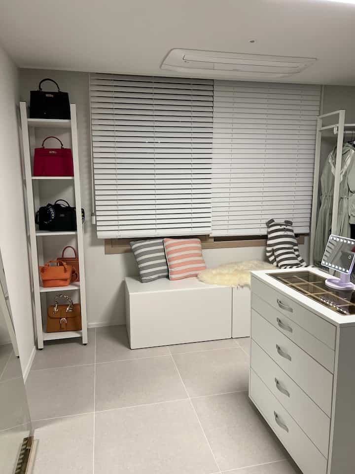 White and simple modern walk-in closet featuring multiple storage units, hangers, and window bench with a clean atmosphere