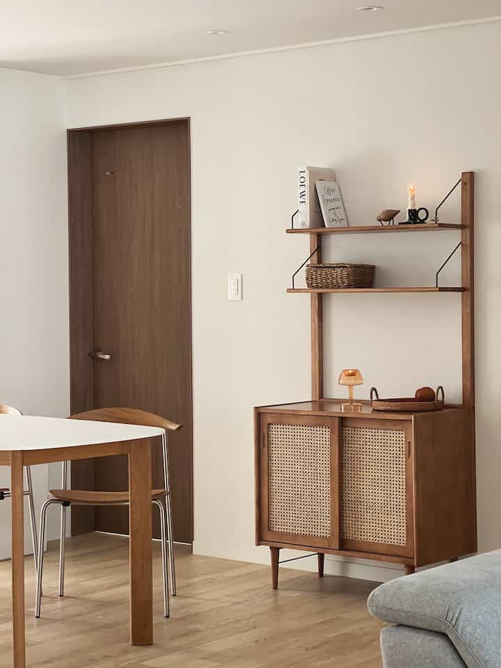 A natural-toned living room with white walls and wooden furniture, featuring tealight holders and simple dining chairs, creating a cozy atmosphere