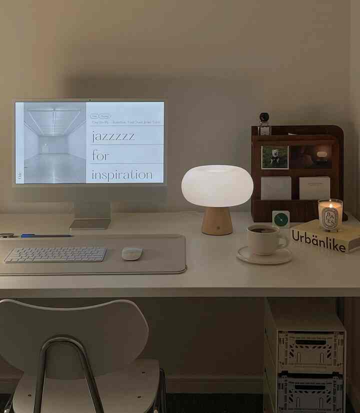 White and brown toned home office space featuring desk with computer, table lamp, and coffee cup in a tidy work setup