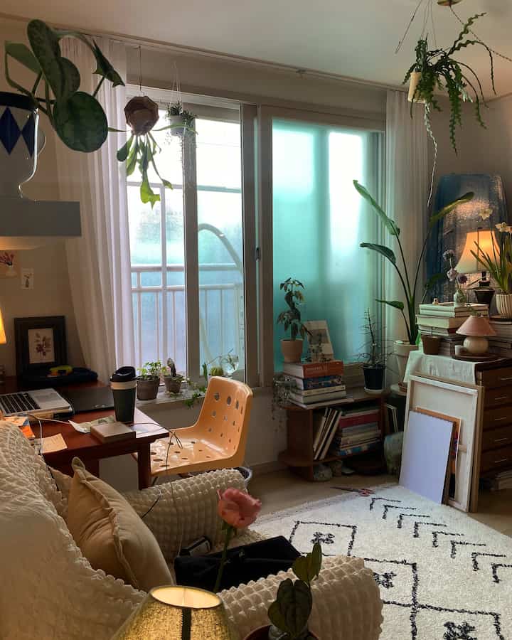 Bright white and wood-toned living room workspace featuring a desk, vintage furnishings, and diverse plants creating a cozy atmosphere