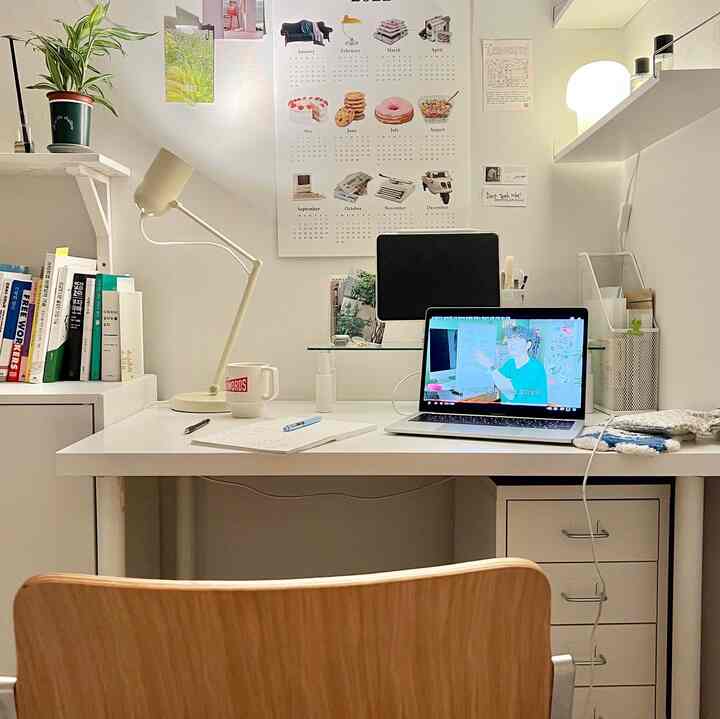 Bright and clean white-toned studio apartment home office featuring desk, chair, and monitor stand.