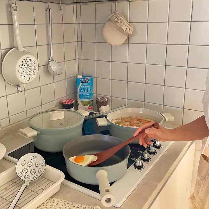 Kitchen with white tiled walls and mint-colored pots, showing a frying pan cooking an egg