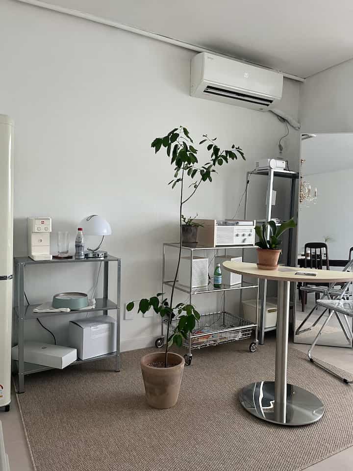 Natural and modern beige-toned space featuring metal storage racks, a round table, and potted plants creating a clean home cafe atmosphere