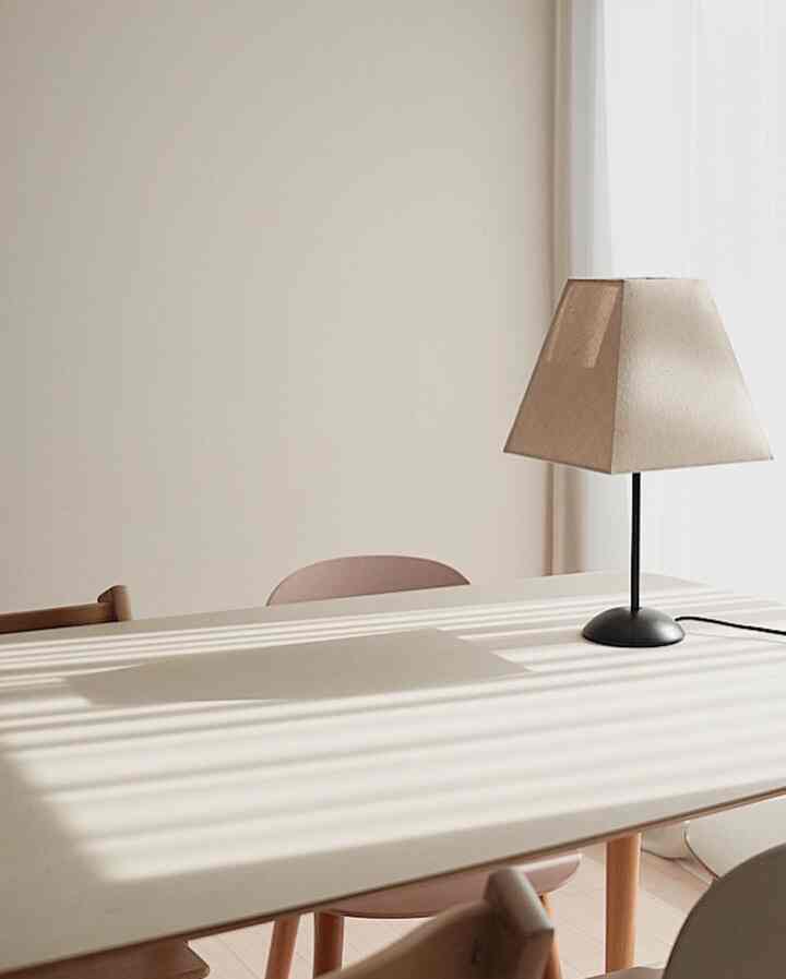 ベージュトーンのシンプルでナチュラルなダイニング空間、テーブル上に置かれたテーブルランプが補助照明として機能するインテリア
