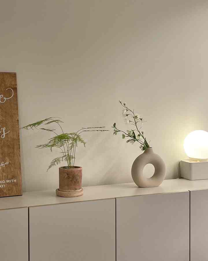 白色のキャビネットの上にテラコッタの鉢と独特な花瓶、ムード照明が配されたシンプルで自然な雰囲気のインテリア