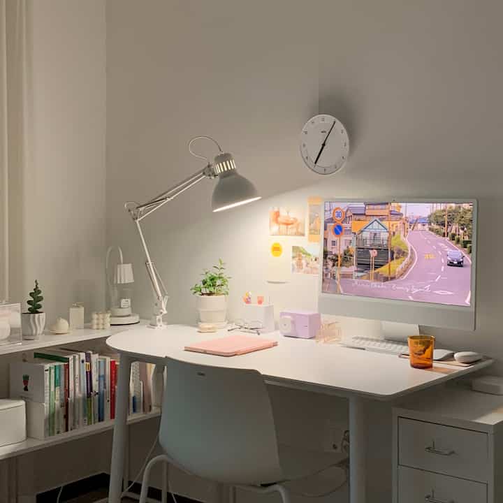 White-tone home office space featuring desk, desk lamp, and iMac with a clean and modern work environment