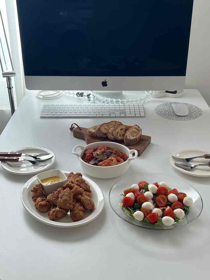 明るいホワイトトーンのホームオフィスデスクに、フレッシュなサラダ、フライドフード、パンが置かれた清潔感のある空間