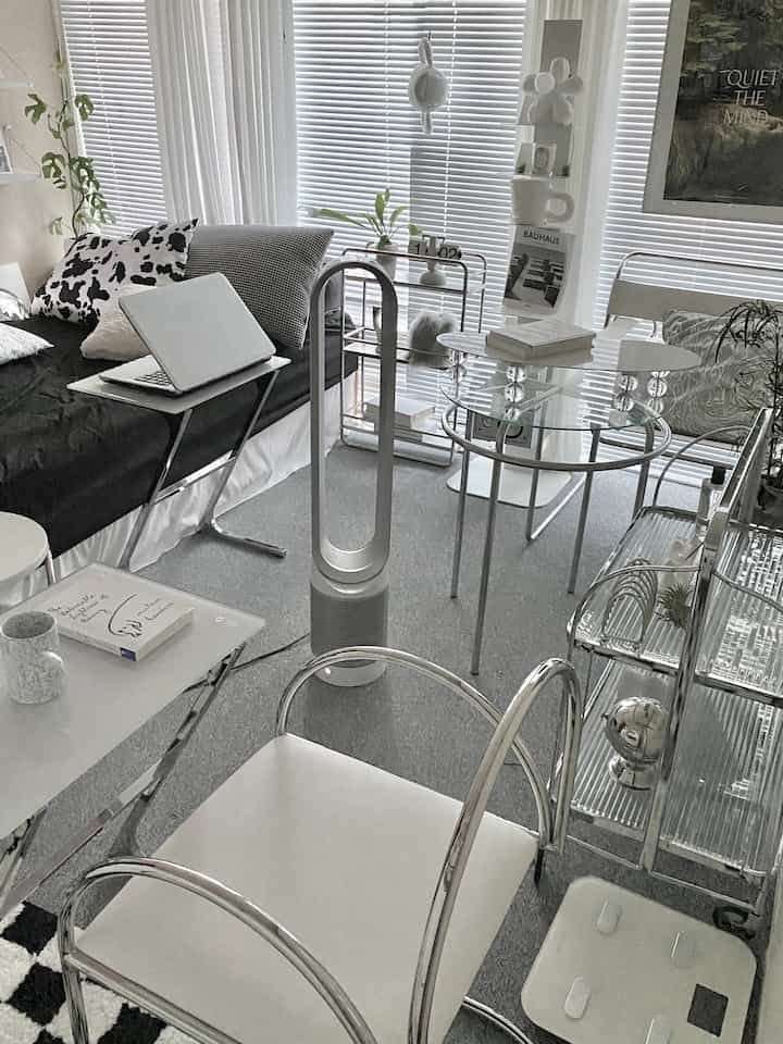 Gray and white toned bedroom featuring modern decor with window blinds, curtains, glass table, and a central air circulator