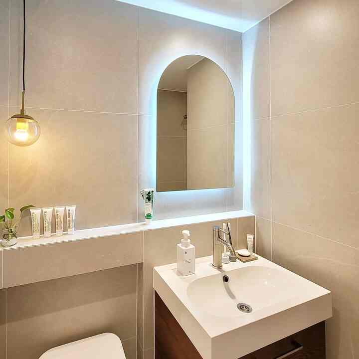 Natural-tone bathroom with arched backlit mirror, sink, and wood cabinet arranged in a clean space