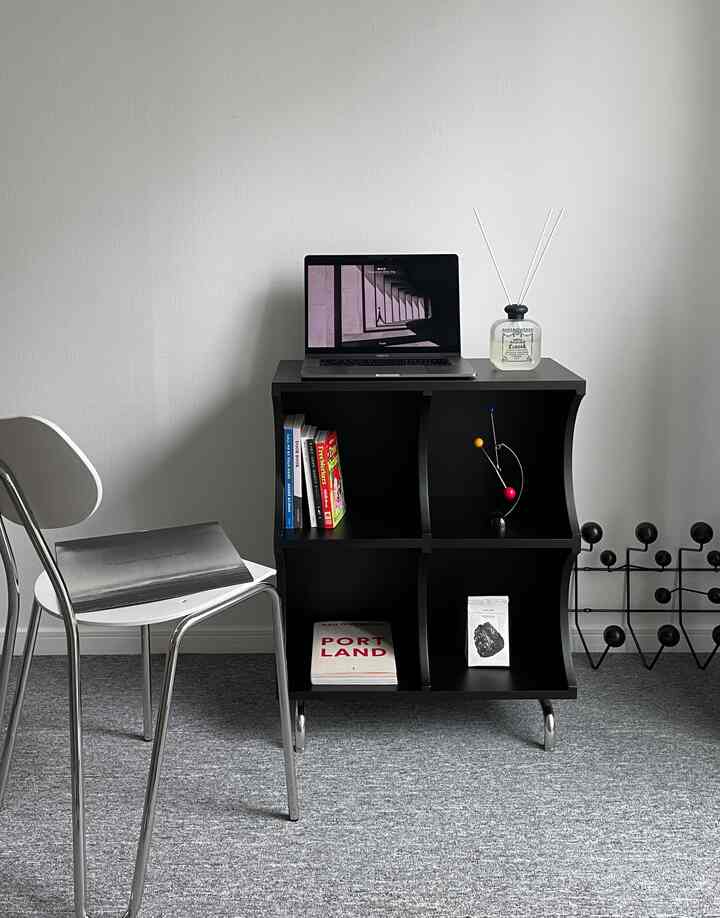 Modern home office space with gray carpet and black modular shelf featuring laptop and minimal decor, clean and sleek atmosphere