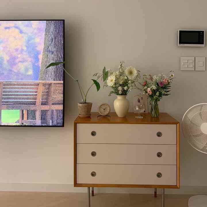 Living room with white walls and brown dresser featuring vases of flowers and a clock, creating a warm modern atmosphere