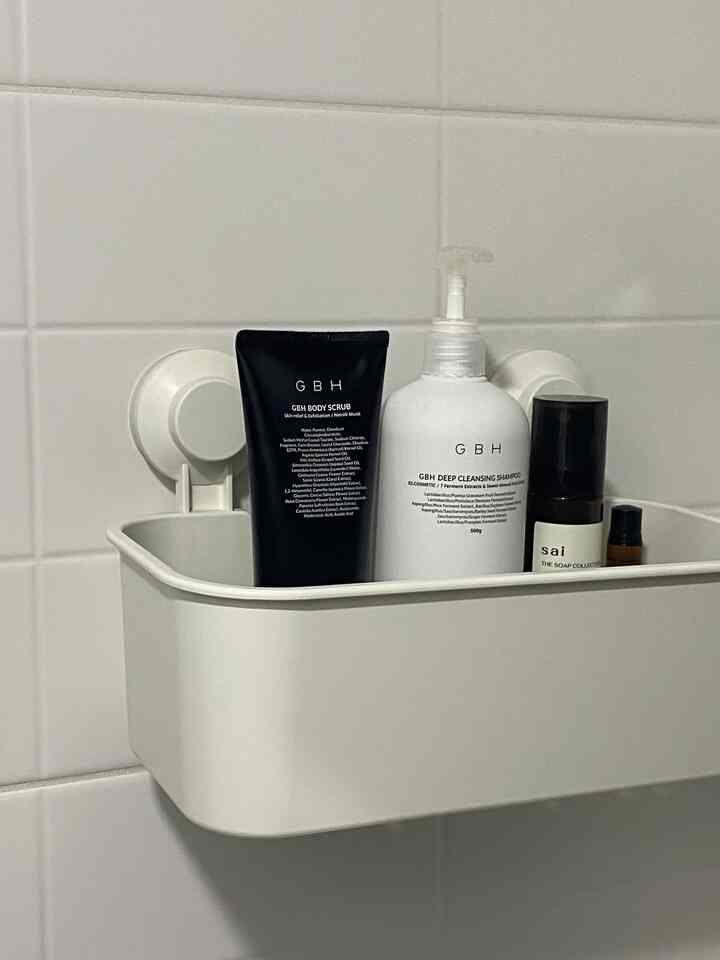 White tiled bathroom wall with a non-drilling suction shelf holding white and black containers, creating a clean and minimal bathroom setting