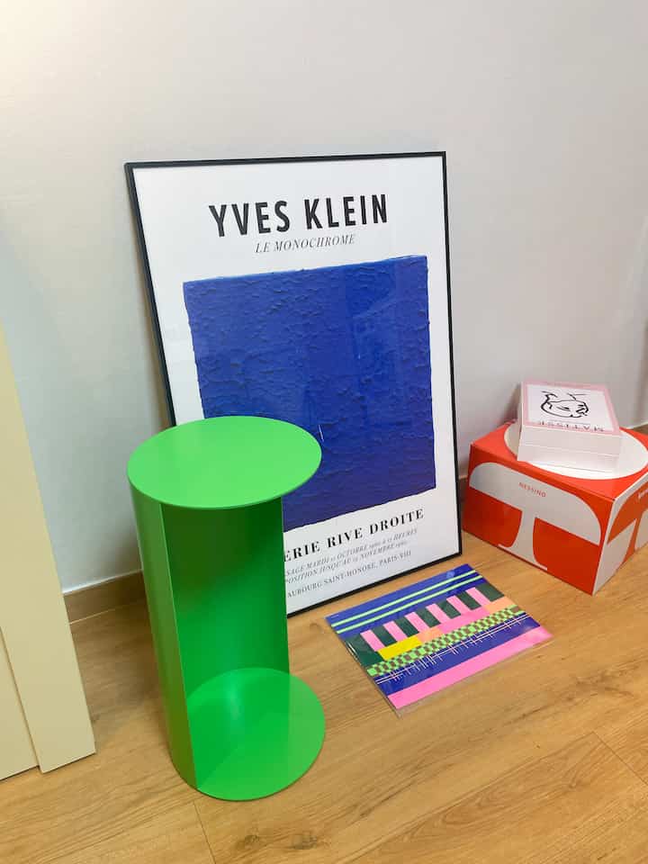 Minimal space with wood tone floor and white walls featuring neon green mini side table and blue picture frame