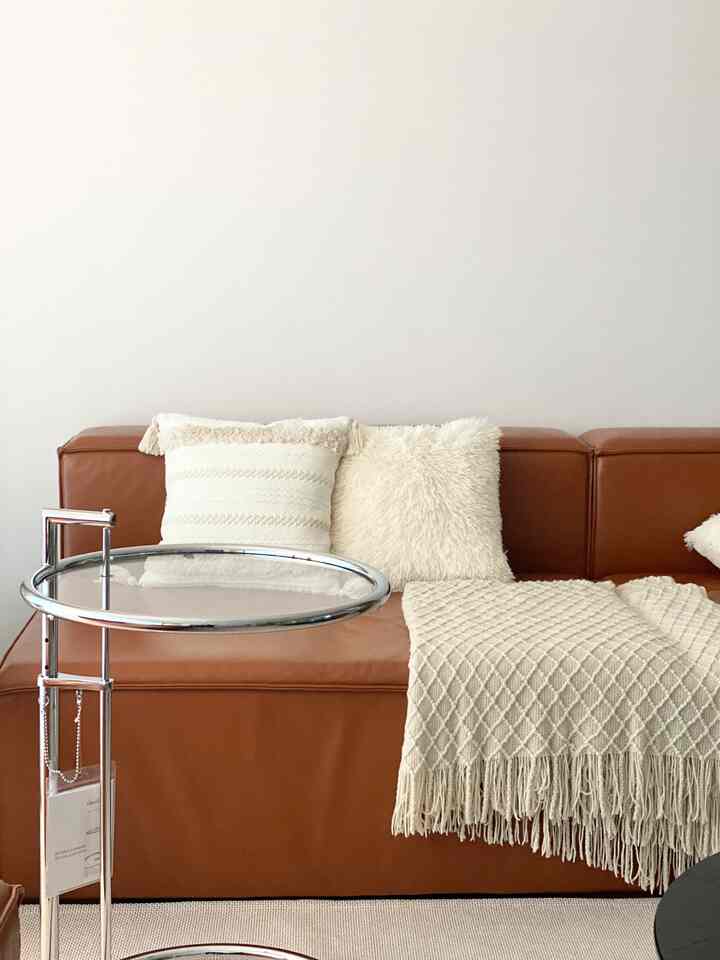 Warm brown leather sofa with beige tone cushions and throw blanket in a natural modern living room space