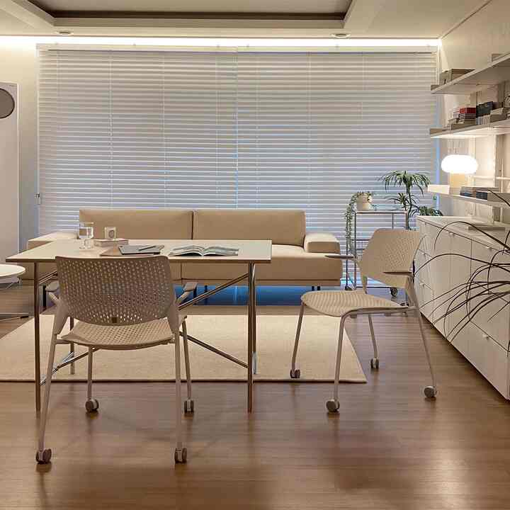 Beige and white toned living room featuring beige sofa, dining table, white blinds, and warm lighting creating a cozy atmosphere