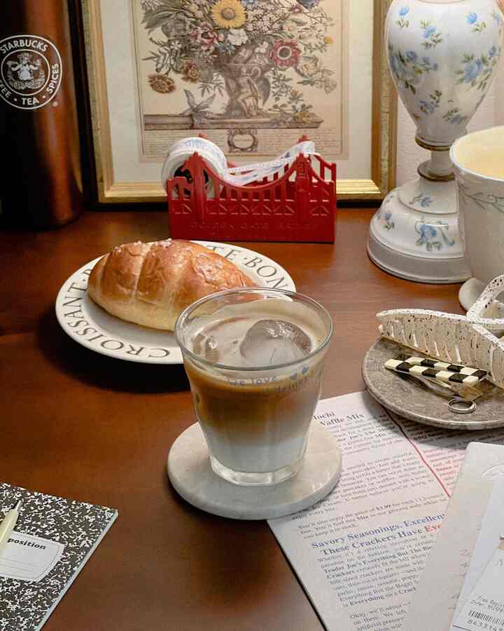 温かみのあるナチュラルカラーのホームカフェ空間、グラスのアイスラテとテーブルに置かれたクロワッサン