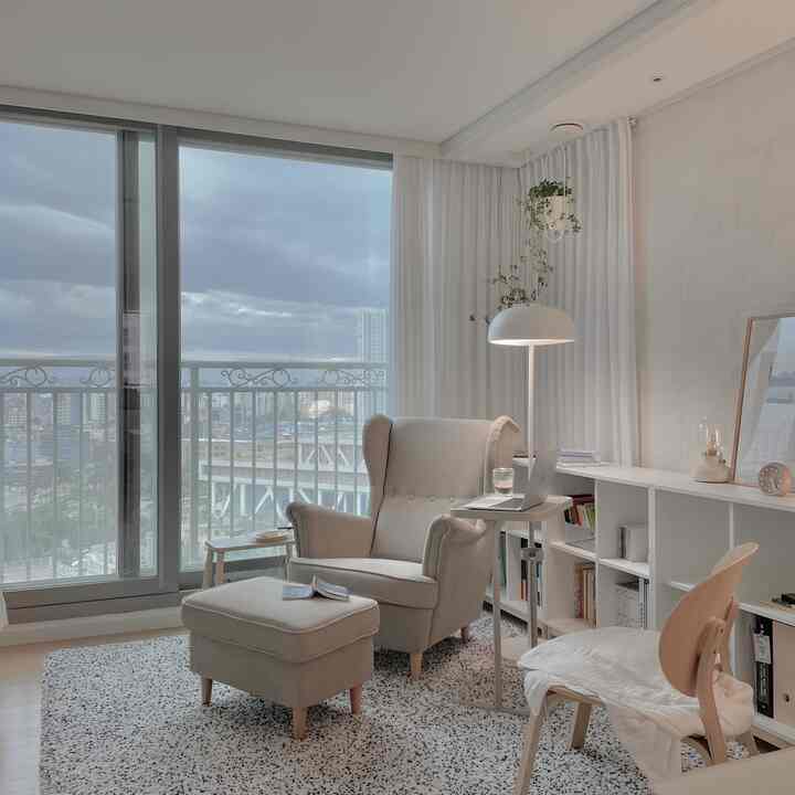 White and natural-toned study-style living room featuring beige armchair and stool on patterned rug, cozy and bright atmosphere
