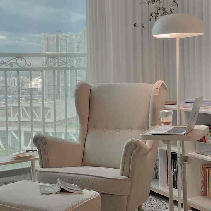 Natural toned modern study-style living room featuring beige armchair and stool with white floor lamp in a cozy setting