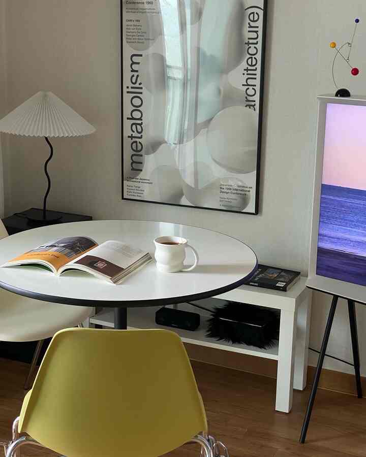 ホワイトと木目調が調和したカフェ風リビング、丸いダイニングテーブルとポスターが配置されたモダンな空間