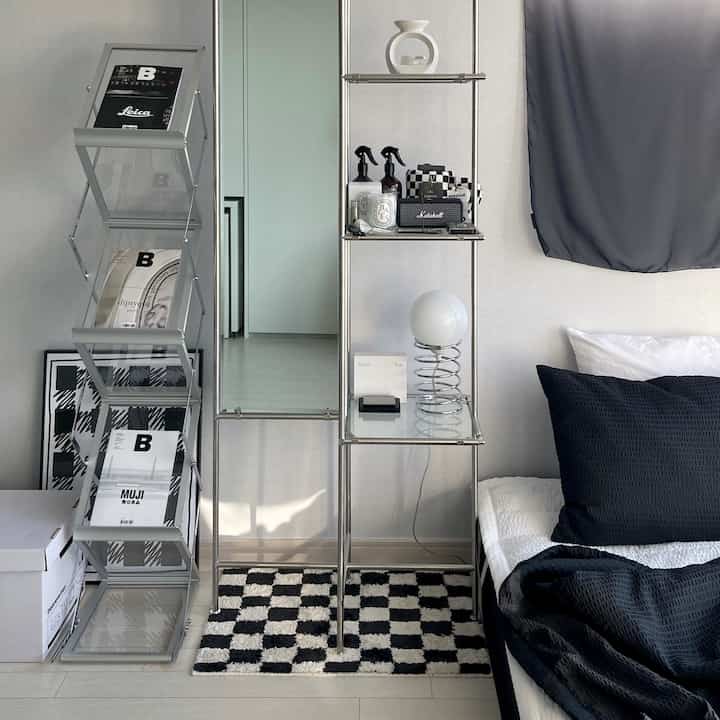 A clean bedroom in white and black monotone featuring Mid-Century Modern racks and a checkerboard rug
