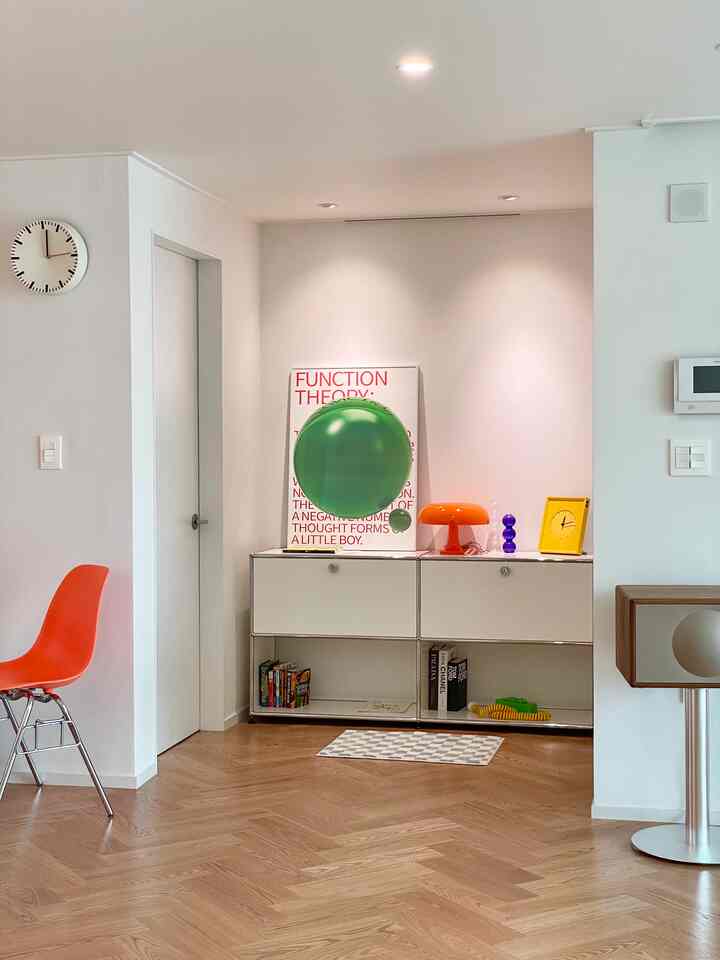Living room with white walls and wood tone flooring, featuring a mid-century modern poster and an orange table lamp in a clean design