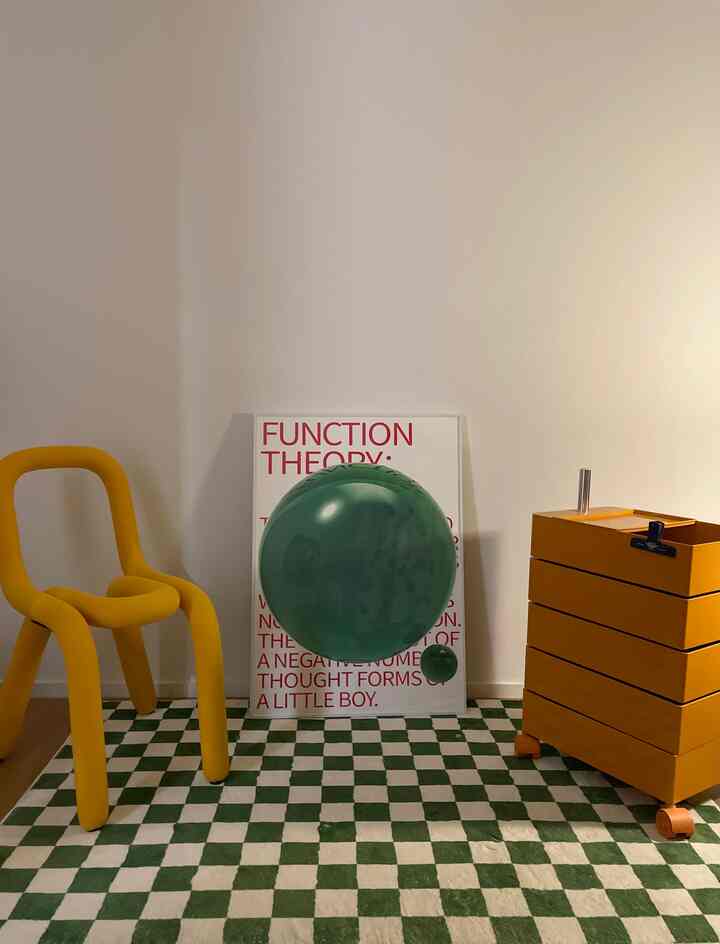 Minimal modern interior with yellow armchair and orange storage cart on navy and white checkerboard rug, featuring a red-lettered poster.