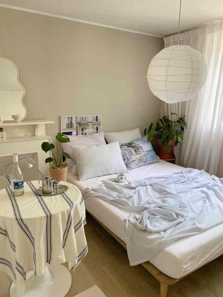 A natural summer bedroom featuring beige walls, a wood tone bed frame with cool blue linen bedding and indoor plants for a fresh atmosphere
