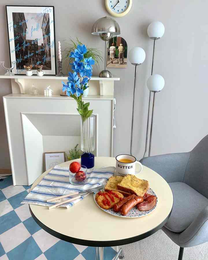 Natural modern dining space with white walls and blue tiled floor, featuring round table with vase of blue flowers and breakfast setup