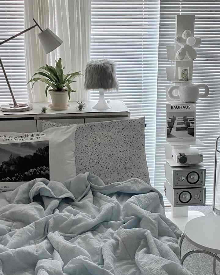 Light gray and white toned studio bedroom featuring bed with pillows, plants, and floor lamp in a simple modern style