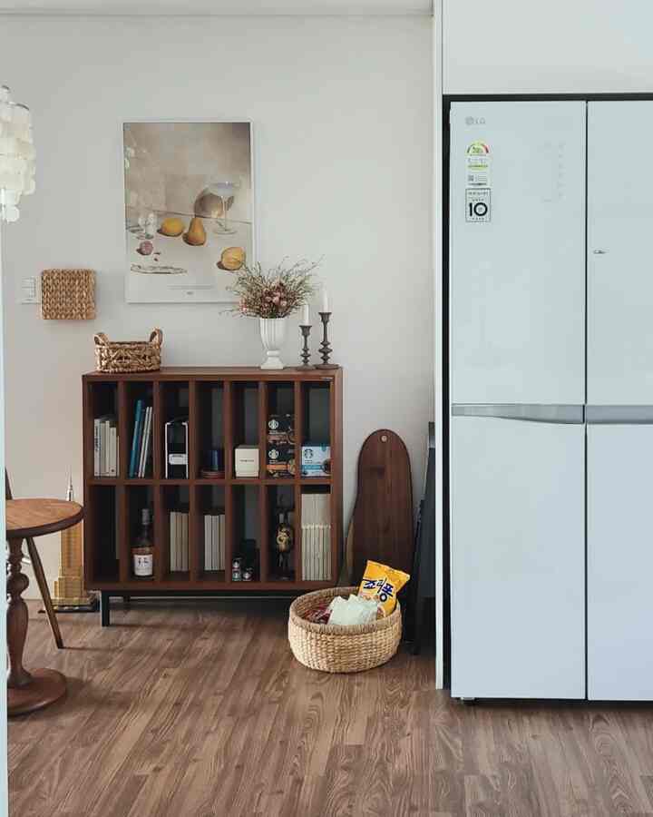 白い壁とブラウンの木製家具が調和したキッチン空間、冷蔵庫とラタンのバスケットが配置された印象的なインテリア