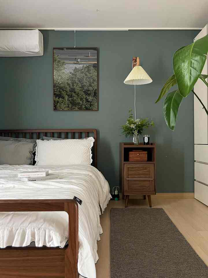 Bedroom with green walls and wood-tone furniture, featuring white bedding and a rug creating a natural atmosphere