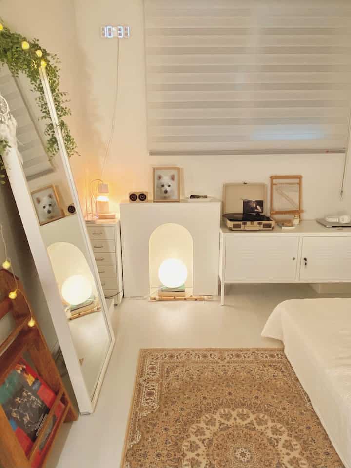 A white and natural toned bedroom featuring cabinets, a rug, and a full-length mirror creating a warm atmosphere