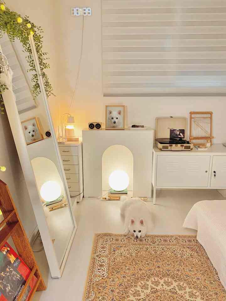 A natural and cozy bedroom in white and beige tones featuring a Persian carpet, full-length mirror, and wall fireplace console decor