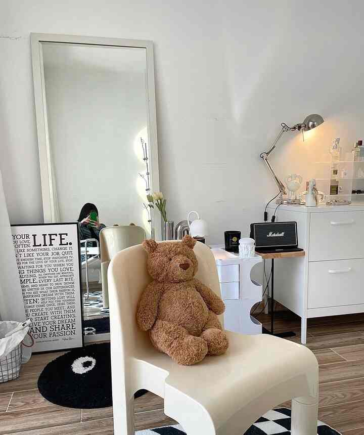 A white and beige mid-century modern home office space featuring a baby teddy bear and cozy decor elements