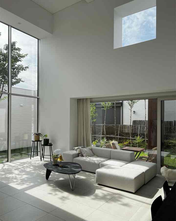 White-toned living room featuring large windows, modern sofa, and coffee table in a bright, neat space