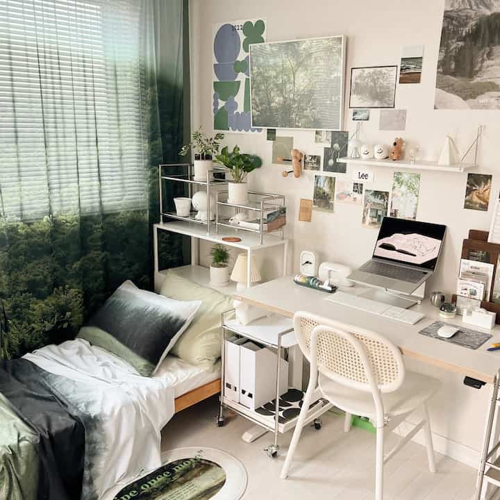 Natural-tone bedroom with green forest-patterned curtains and bedding, featuring a white desk and chair in a cozy home office setup