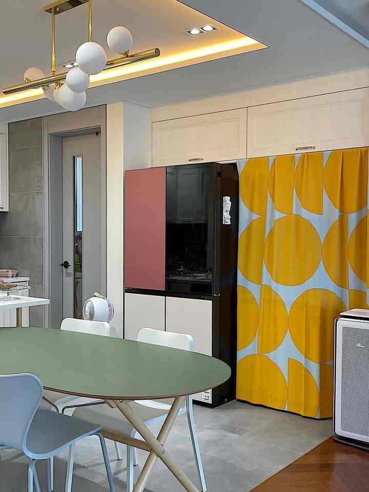 白と黄色のトーンのキッチンダイニングルーム、緑のダイニングテーブルと印象的なカーテンが配置されたモダンな空間