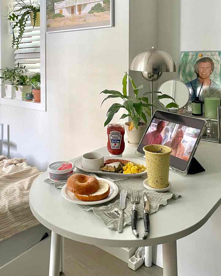 白を基調としたワンルーム、円形のダイニングテーブルと自然植物、照明、朝食が配置された落ち着いた雰囲気のインテリア