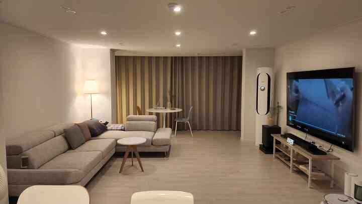 Modern living room in white tones featuring a large sofa, round dining table, and wall-mounted TV with a calm atmosphere