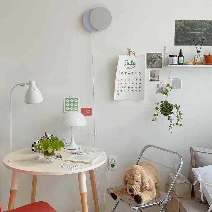 A small white and natural-toned room featuring a round table, reading lamps, and a plush dog toy creating a tidy home office setup