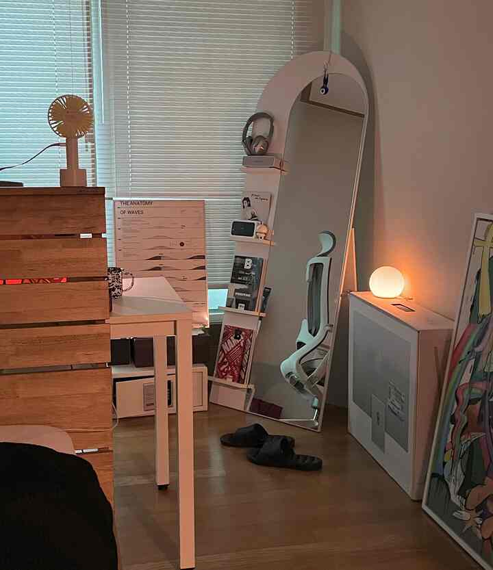 A white and wood tone studio bedroom featuring an arched full-length mirror and desk in a neat arrangement