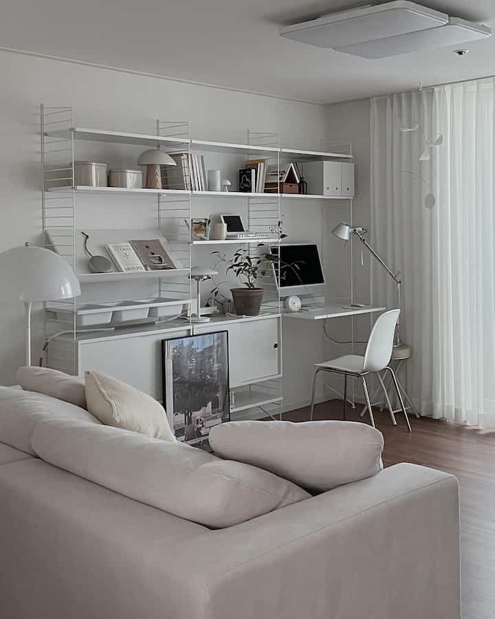White-toned study living room featuring modern sofa, bookshelf, and computer desk in a neat, minimalist space