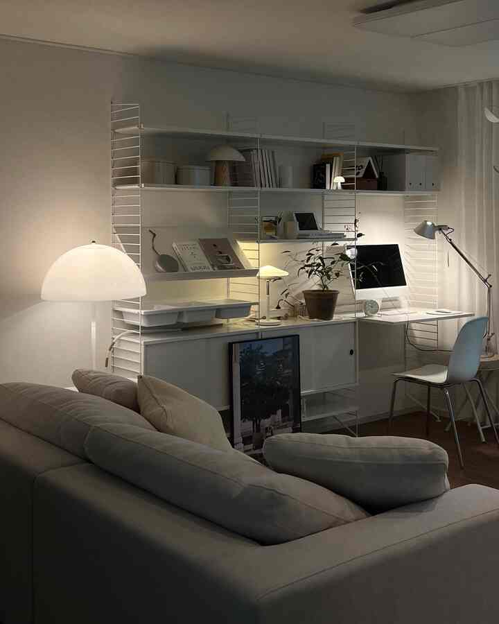 A compact living room and home office space in white and beige tones, featuring modern furniture and multiple lighting elements for a cozy atmosphere