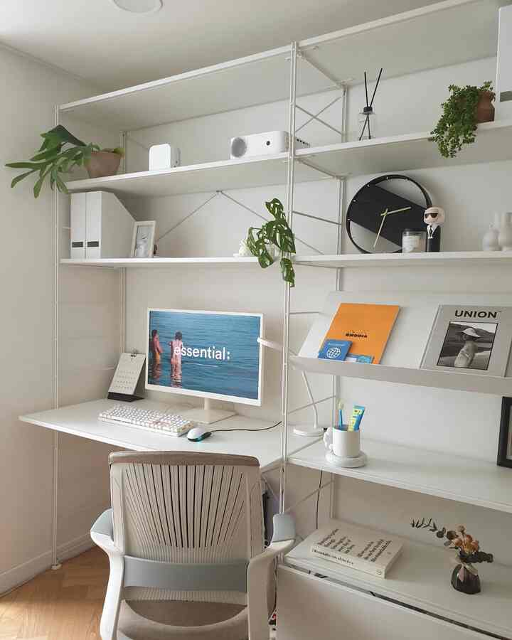 White and natural tone home office study featuring a tidy desk and shelves with books and plants creating a calm atmosphere