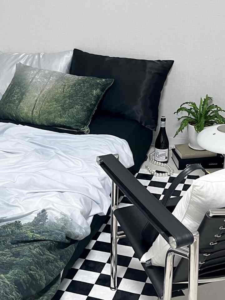 Bedroom with black and white checkerboard rug, natural-themed bedding and pillows, modern armchair creating a simple and natural atmosphere