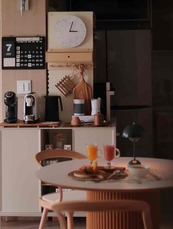 Natural color kitchen space featuring a round dining table, coffee machines, and wall clock creating a cozy home cafe atmosphere