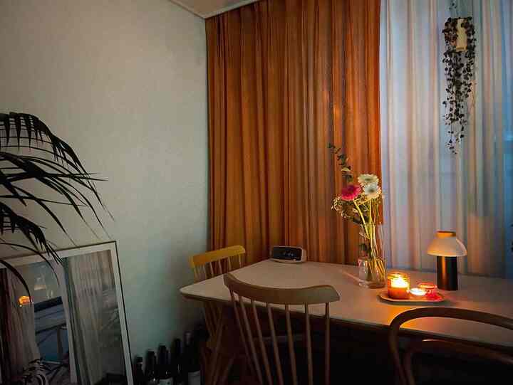 Cozy living room dining space with warm orange curtains and candles on table, wooden chairs arranged in cafe style interior